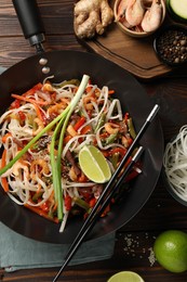 Photo of Shrimp stir fry with noodles and vegetables in wok on wooden table, flat lay