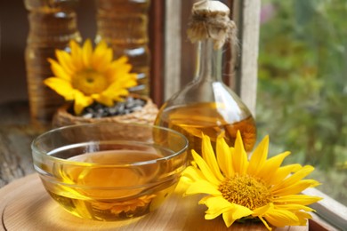 Photo of Organic sunflower oil and flower on wooden board, closeup