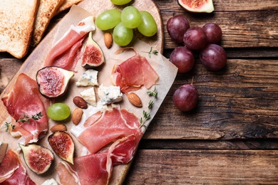 Photo of Ripe figs and prosciutto served on wooden table, flat lay