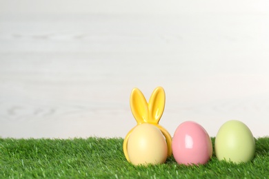 Photo of Cute dyed eggs with decorative Easter bunny ears on green grass, space for text