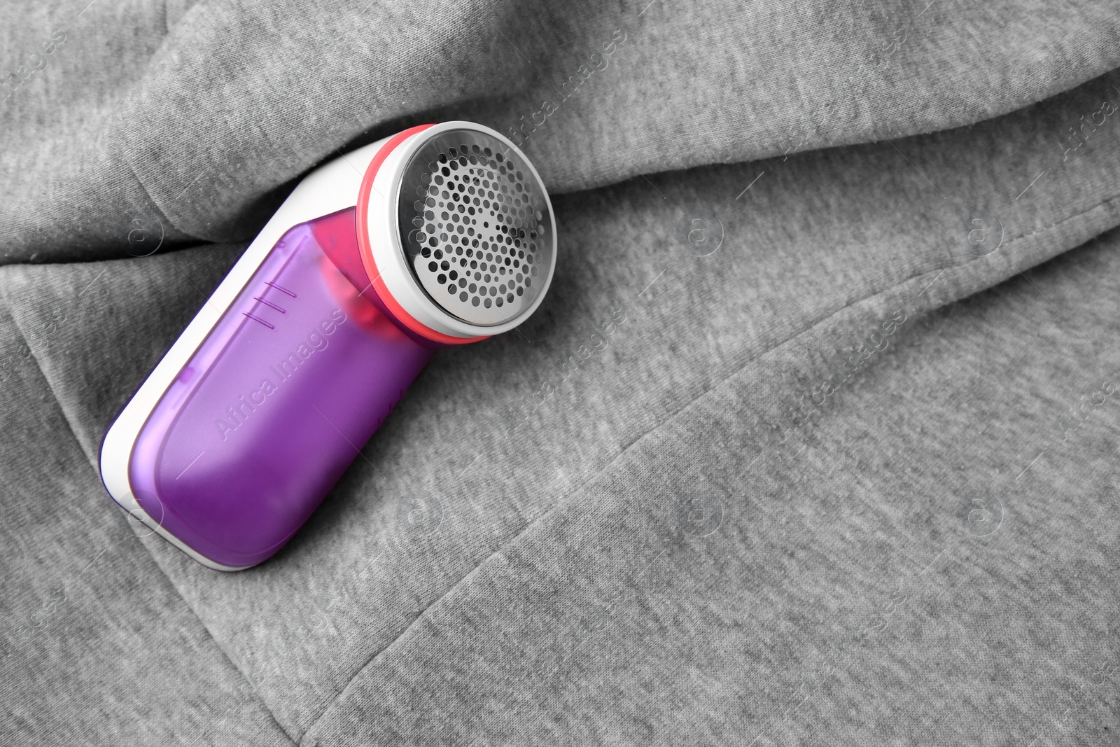 Photo of Modern fabric shaver on light grey cloth with lint, above view. Space for text