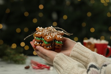 Photo of Woman with decorated cookies against blurred Christmas lights, closeup