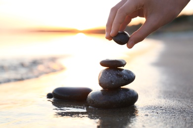 Photo of Woman stacking dark stones on sand near sea, space for text. Zen concept