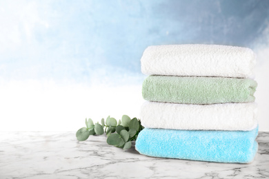 Photo of Stack of clean soft bath towels and green branch on white marble table. Space for text