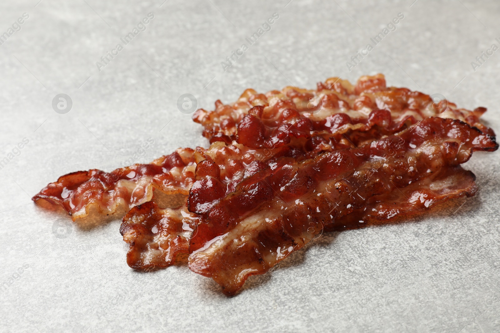 Photo of Pieces of tasty fried bacon on gray textured table, closeup