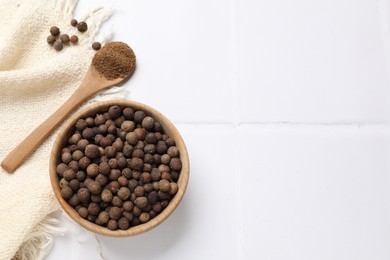 Photo of Ground and whole allspice berries (Jamaica pepper) on white tiled table, top view. Space for text