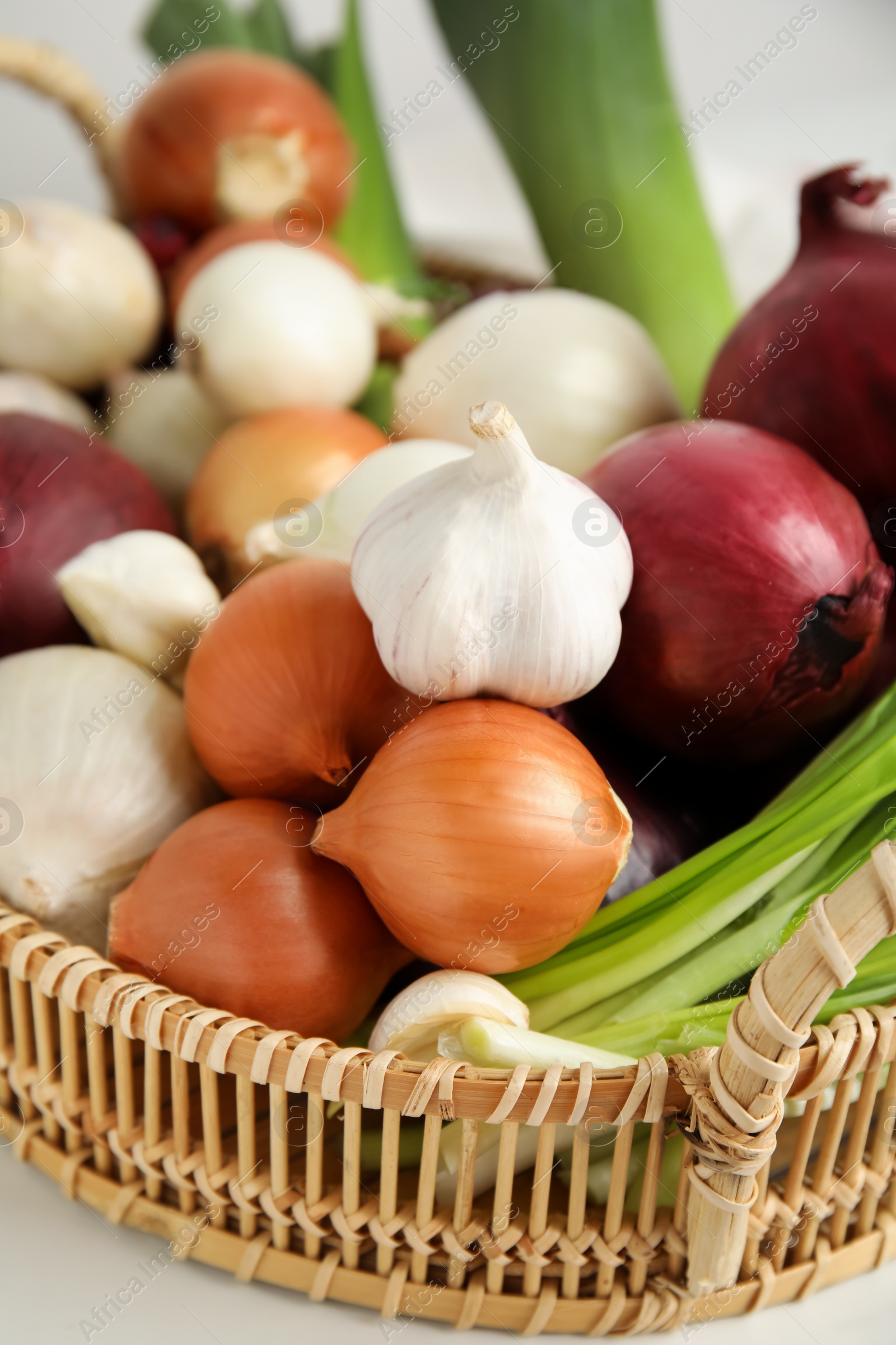 Photo of Wicker tray with fresh onions and garlic on white table, closeup