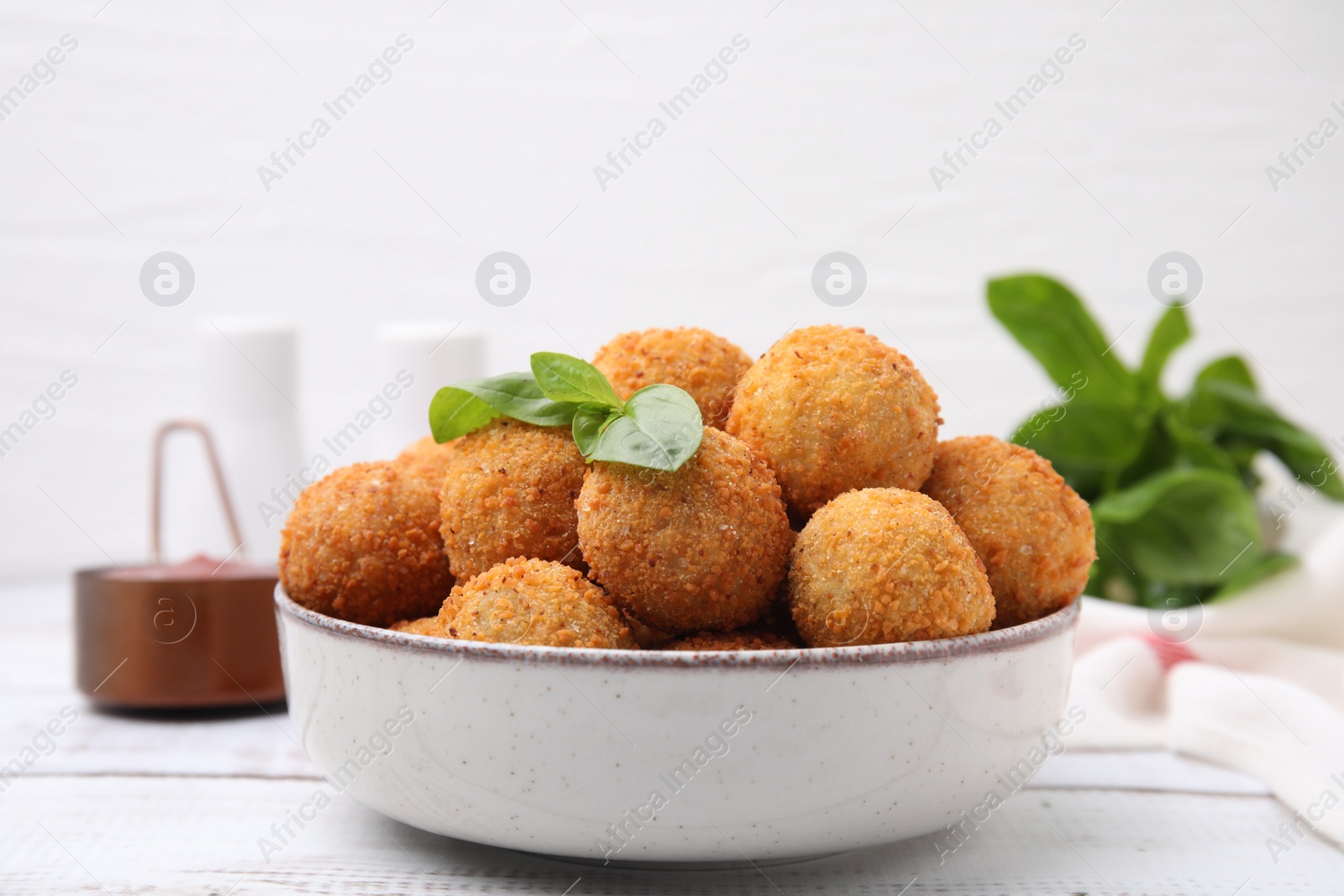 Photo of Bowl of delicious fried tofu balls with basil on white wooden table