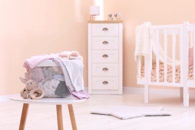 Laundry basket with baby clothes and crochet toys on white wooden table in child room, space for text