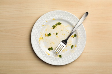 Dirty plate with food leftovers and fork on wooden background, top view