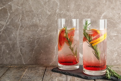 Photo of Glasses of fresh grapefruit cocktail with rosemary and space for text on color background