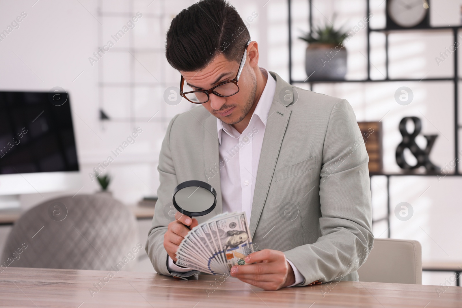 Photo of Expert authenticating 100 dollar banknotes with magnifying glass at table in office. Fake money concept