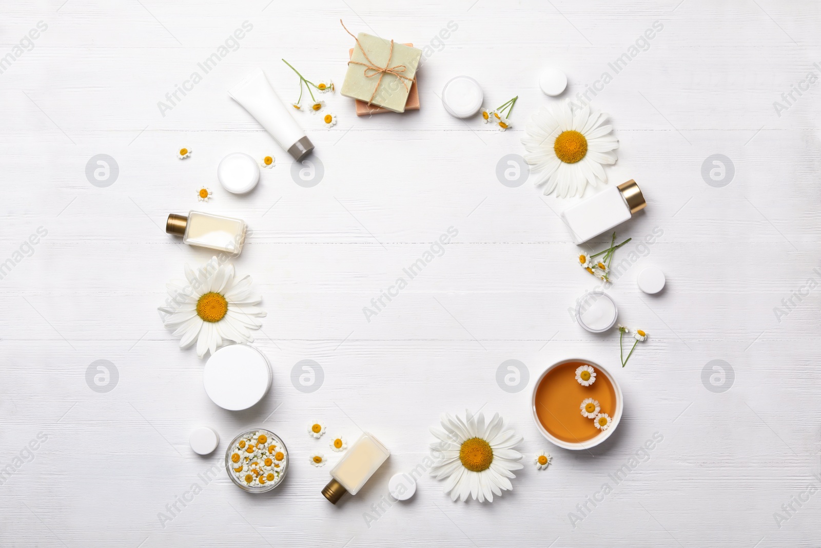 Photo of Frame of chamomile flowers and cosmetic products on white wooden table, flat lay. Space for text