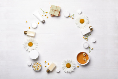 Frame of chamomile flowers and cosmetic products on white wooden table, flat lay. Space for text