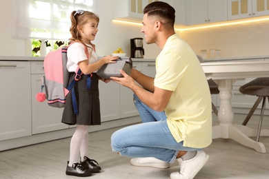Photo of Father helping his little child get ready for school in kitchen