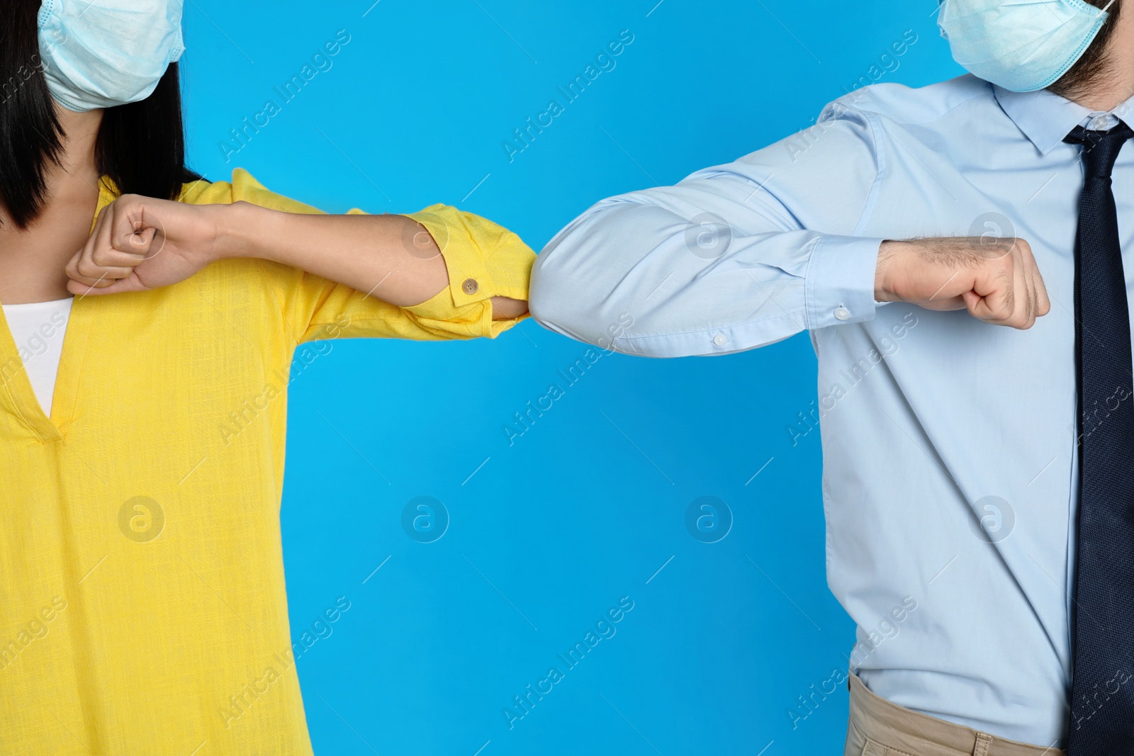 Photo of Man and woman bumping elbows to say hello on light blue background, closeup. Keeping social distance during coronavirus pandemic