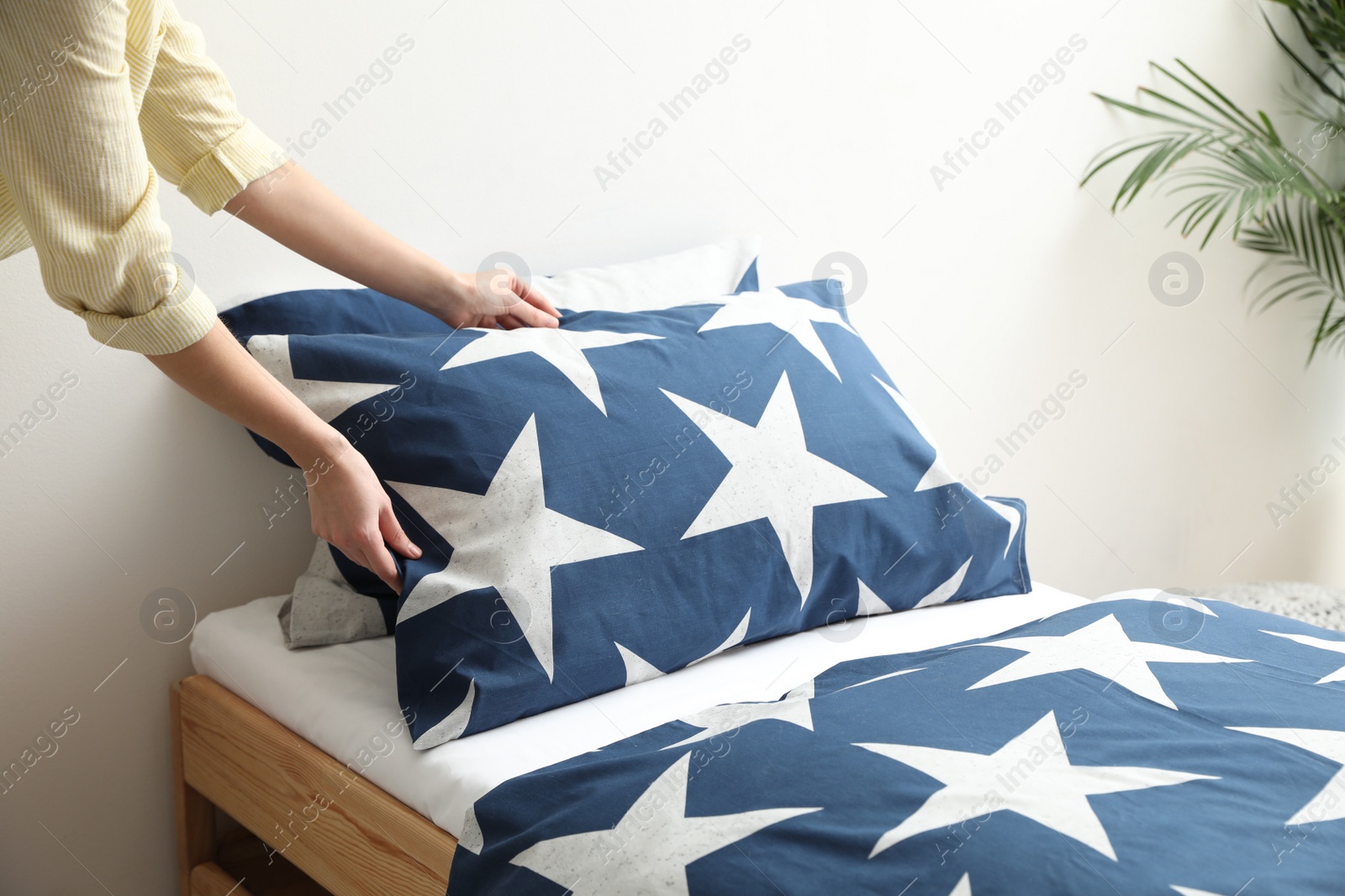 Photo of Woman making bed with stylish linens in children's room, closeup