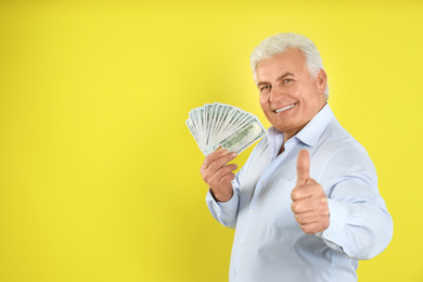 Photo of Happy senior man with cash money on yellow background. Space for text