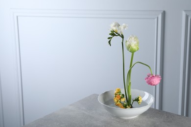 Stylish ikebana as house decor. Beautiful fresh flowers on grey table near white wall, space for text