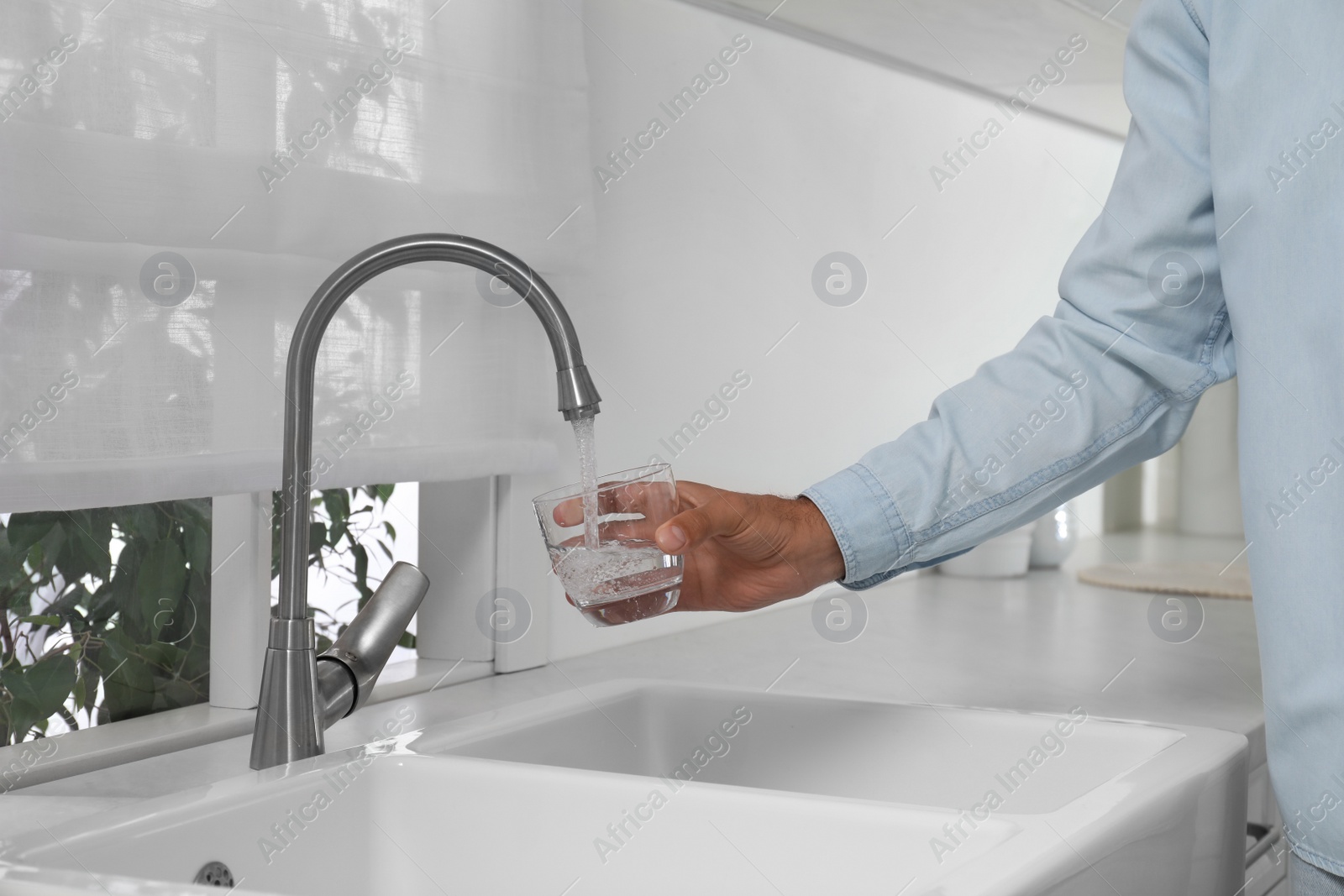 Photo of Man filling glass with water from tap in kitchen, closeup