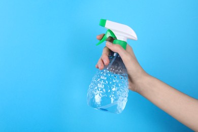 Photo of Woman holding plastic spray bottle on light blue background, closeup. Space for text