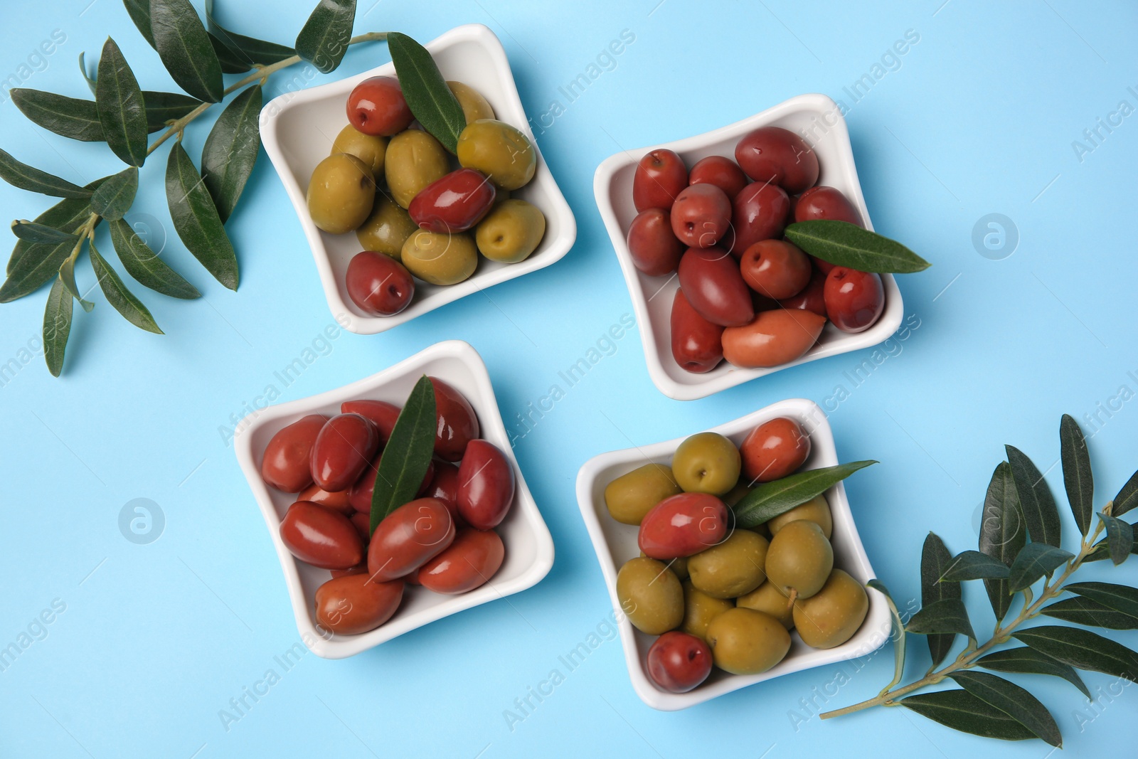 Photo of Different fresh olives and green leaves on light blue background, flat lay