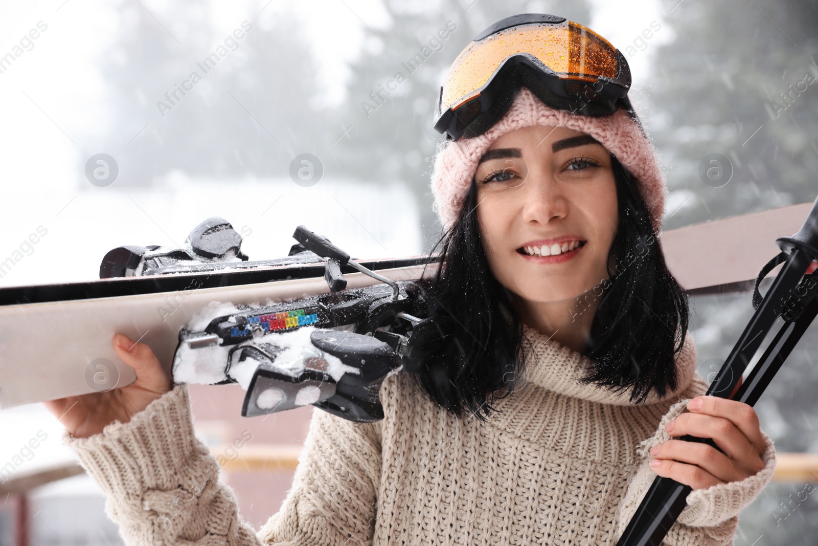 Photo of Young woman with skis wearing winter sport clothes and goggles outdoors