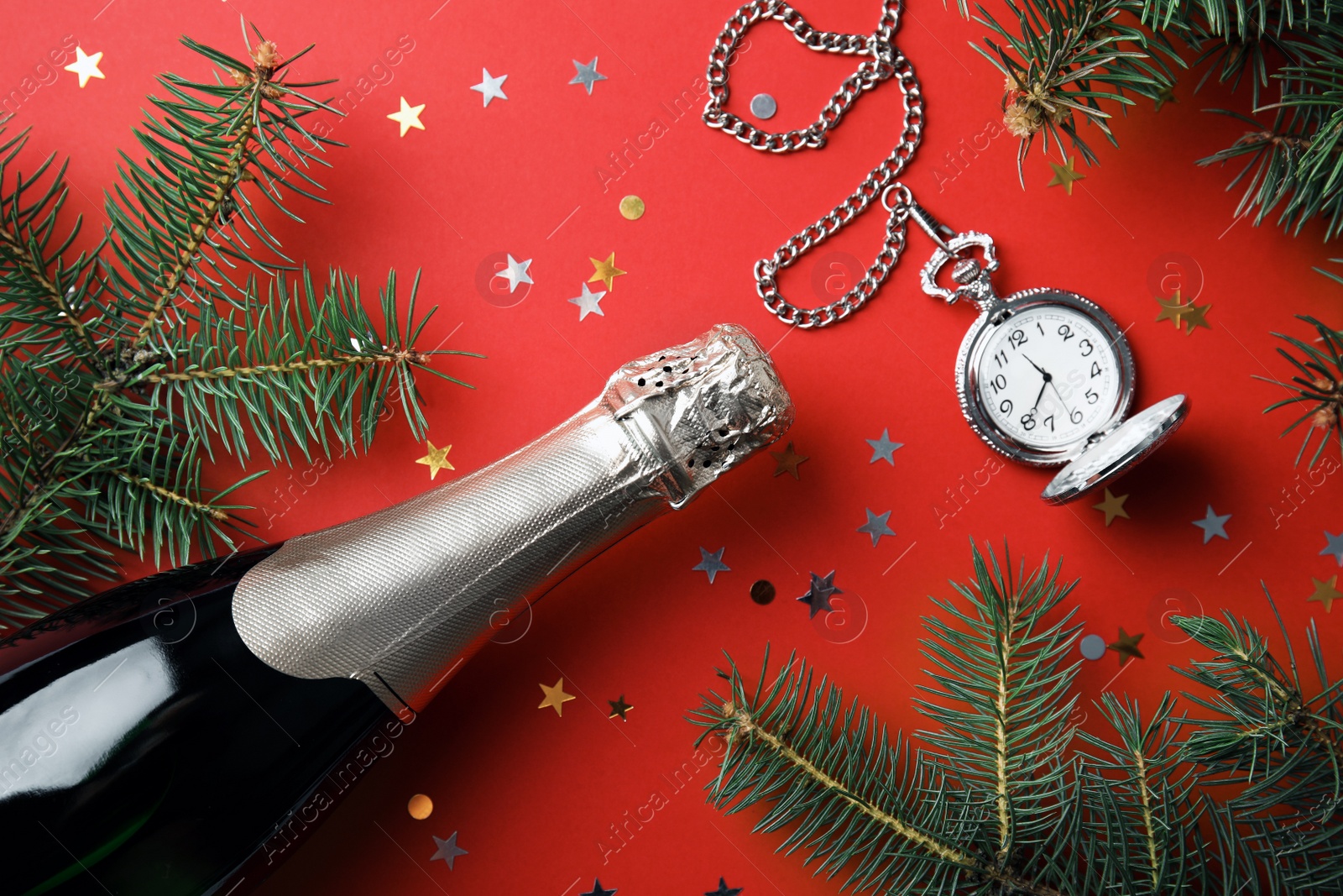 Photo of Christmas composition with bottle of champagne, pocket watch and fir tree branches on red background, top view