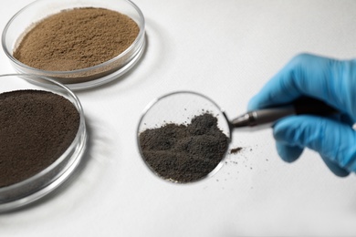 Photo of Scientist examining soil sample with magnifier at table, closeup. Laboratory research