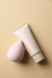 Makeup sponges and skin foundation on beige background, top view