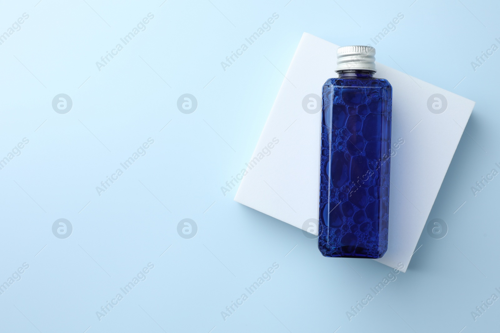 Photo of Bottle of cosmetic product on light blue background, top view. Space for text