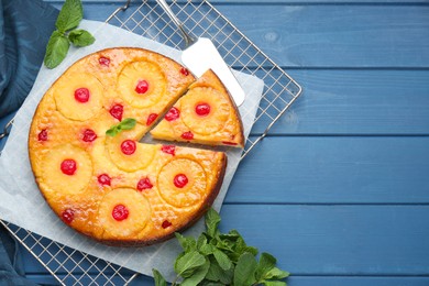 Photo of Delicious cut pineapple pie with cherry and mint on blue wooden table, flat lay. Space for text