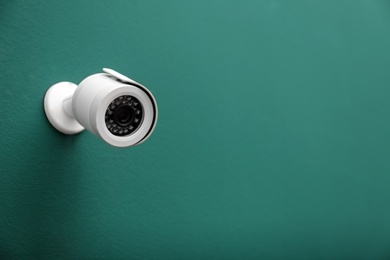 Photo of Modern CCTV security camera on green wall. Space for text