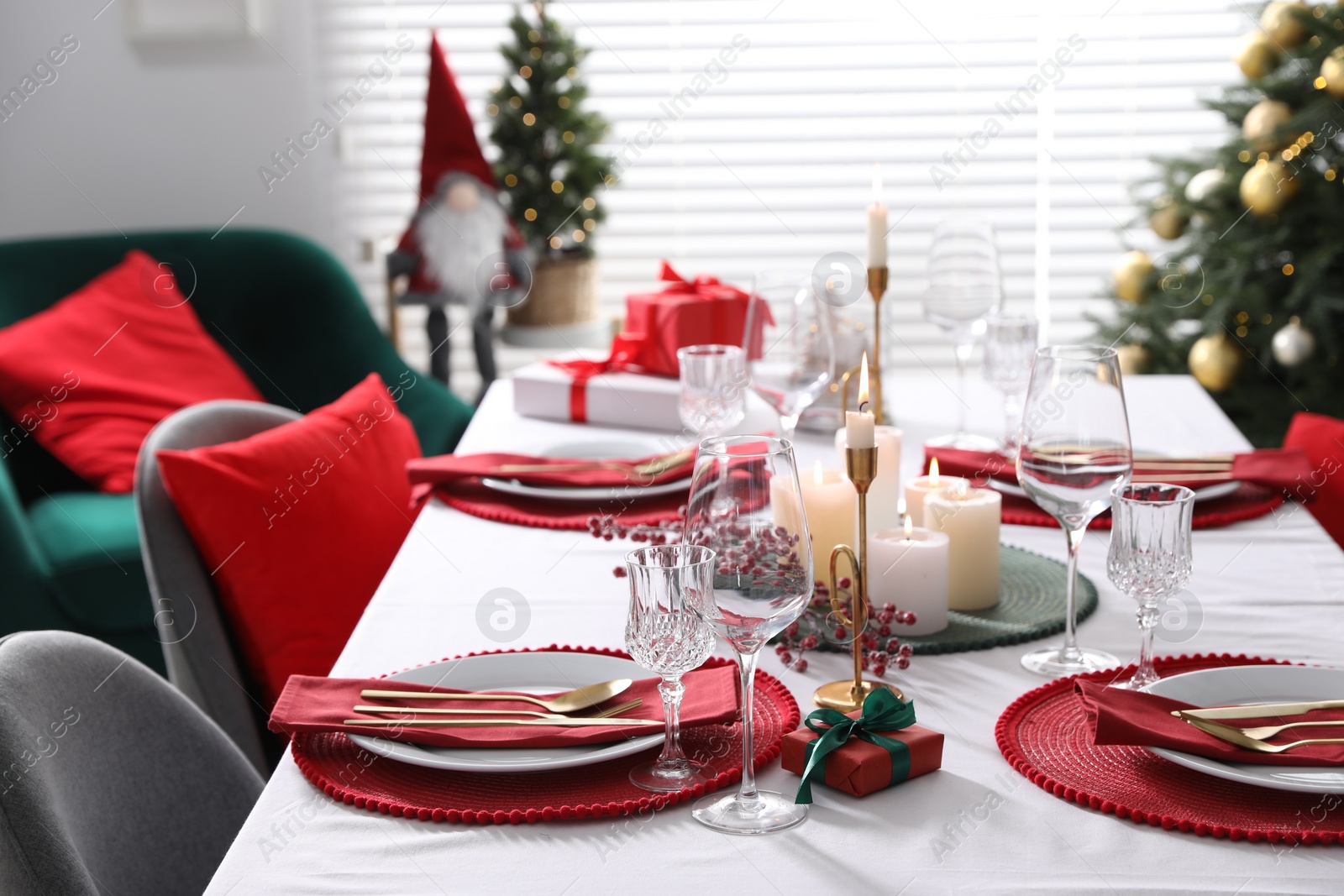 Photo of Christmas table setting with burning candles, gift box and dishware indoors