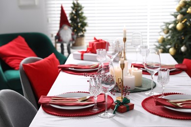 Christmas table setting with burning candles, gift box and dishware indoors