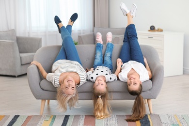Portrait of young woman, her mature mother and daughter lying upside down on sofa in living room