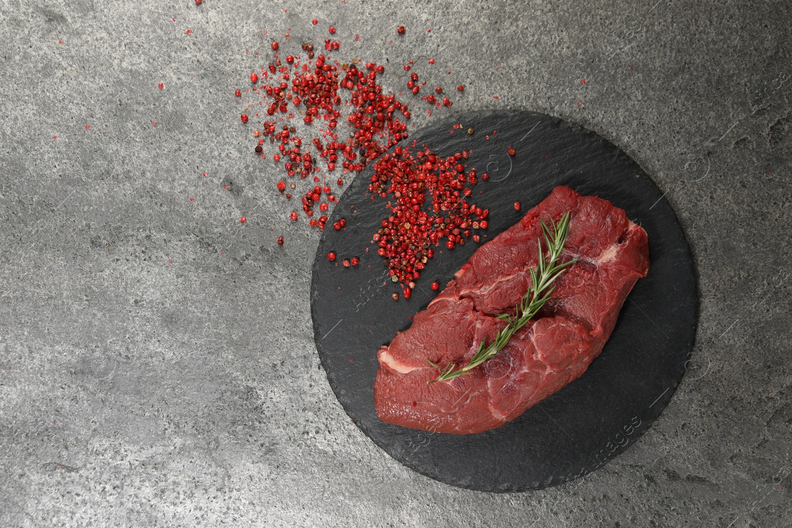 Photo of Piece of raw beef meat, rosemary and red peppercorns on grey table, flat lay. Space for text