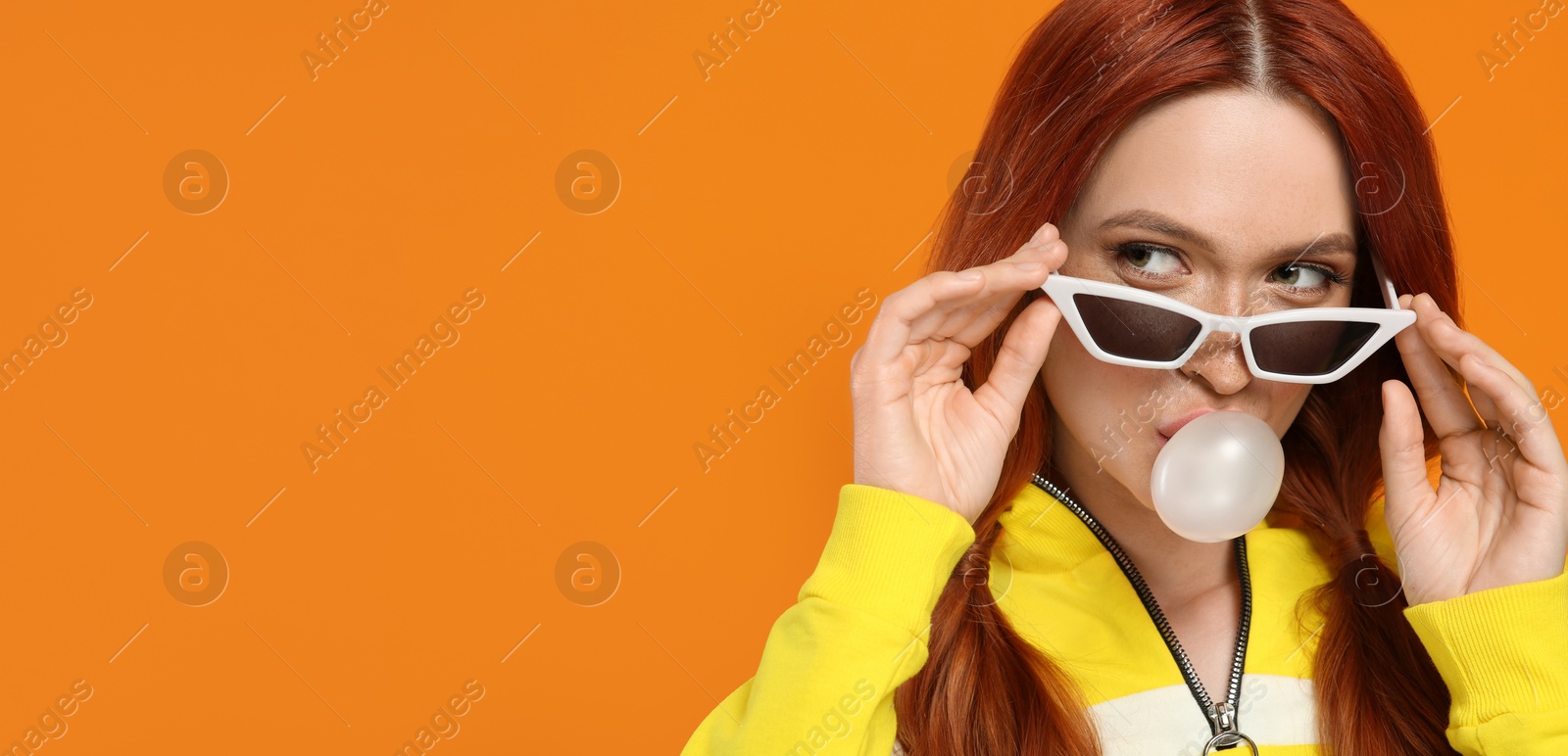 Photo of Beautiful woman in sunglasses blowing bubble gum on orange background. Space for text