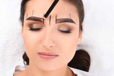 Photo of Cosmetologist preparing young woman for  eyebrow permanent makeup procedure, closeup