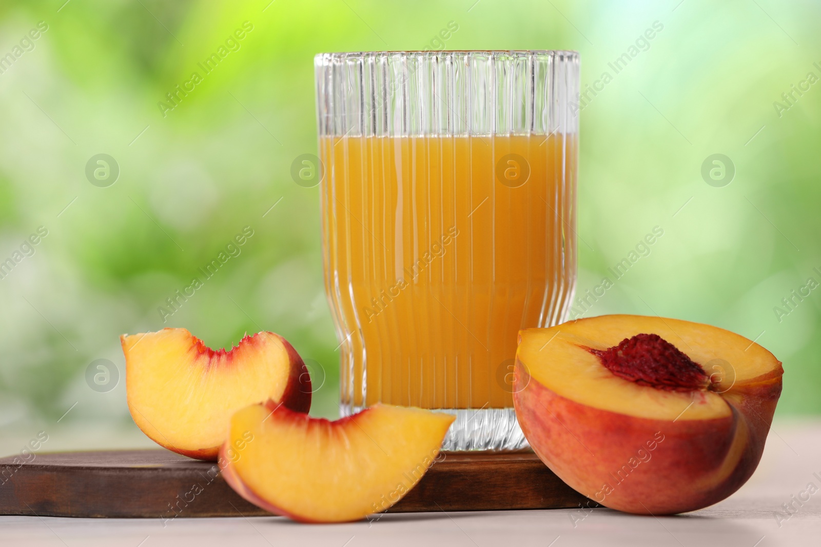 Photo of Glass of tasty peach juice and fresh fruit on white table outdoors, closeup