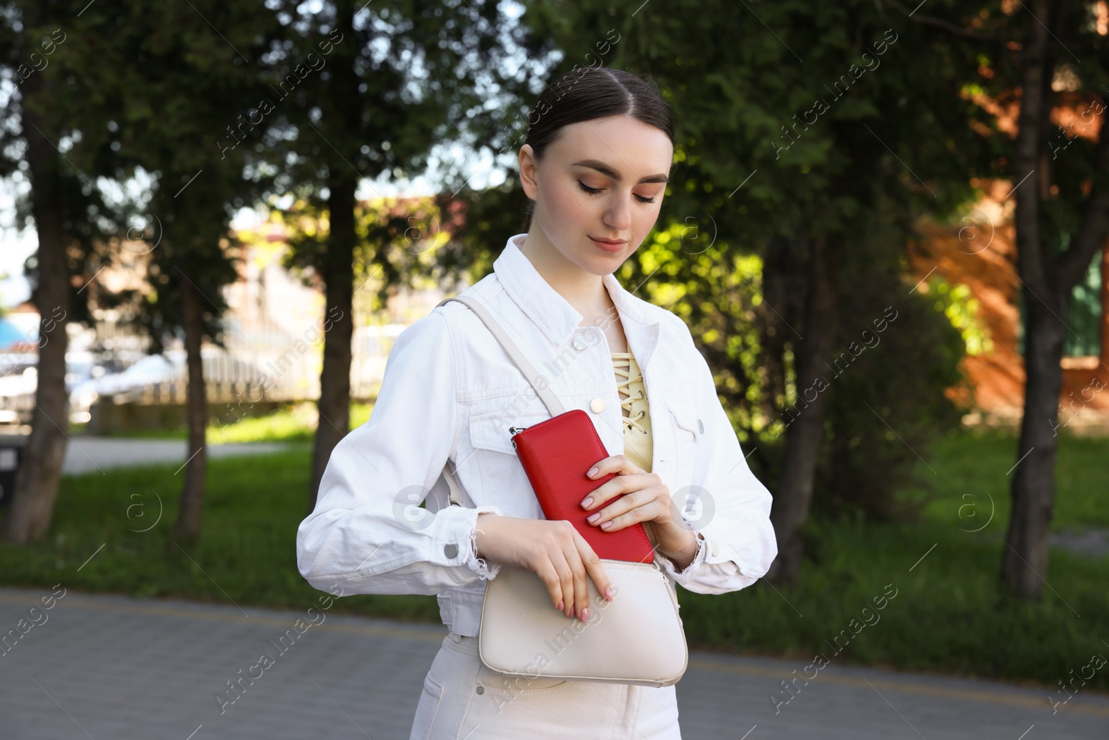 Photo of Young woman putting purse into bag outdoors