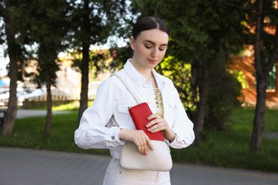 Young woman putting purse into bag outdoors