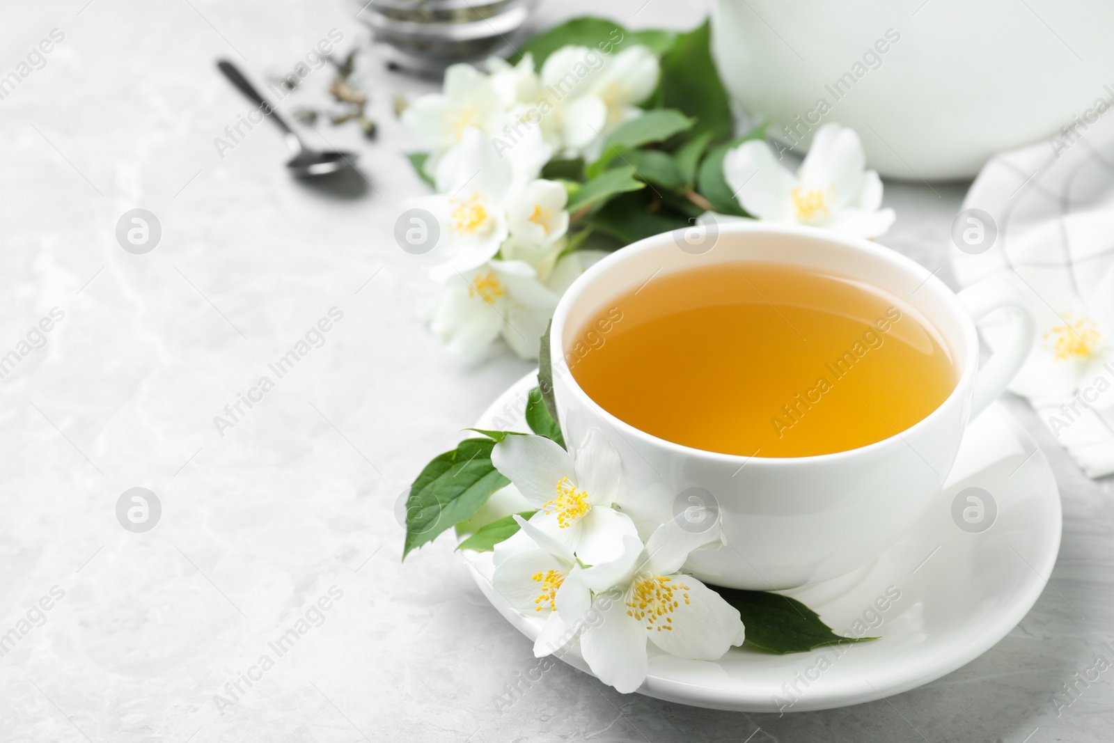 Photo of Cup of tea and fresh jasmine flowers on light grey marble table. Space for text