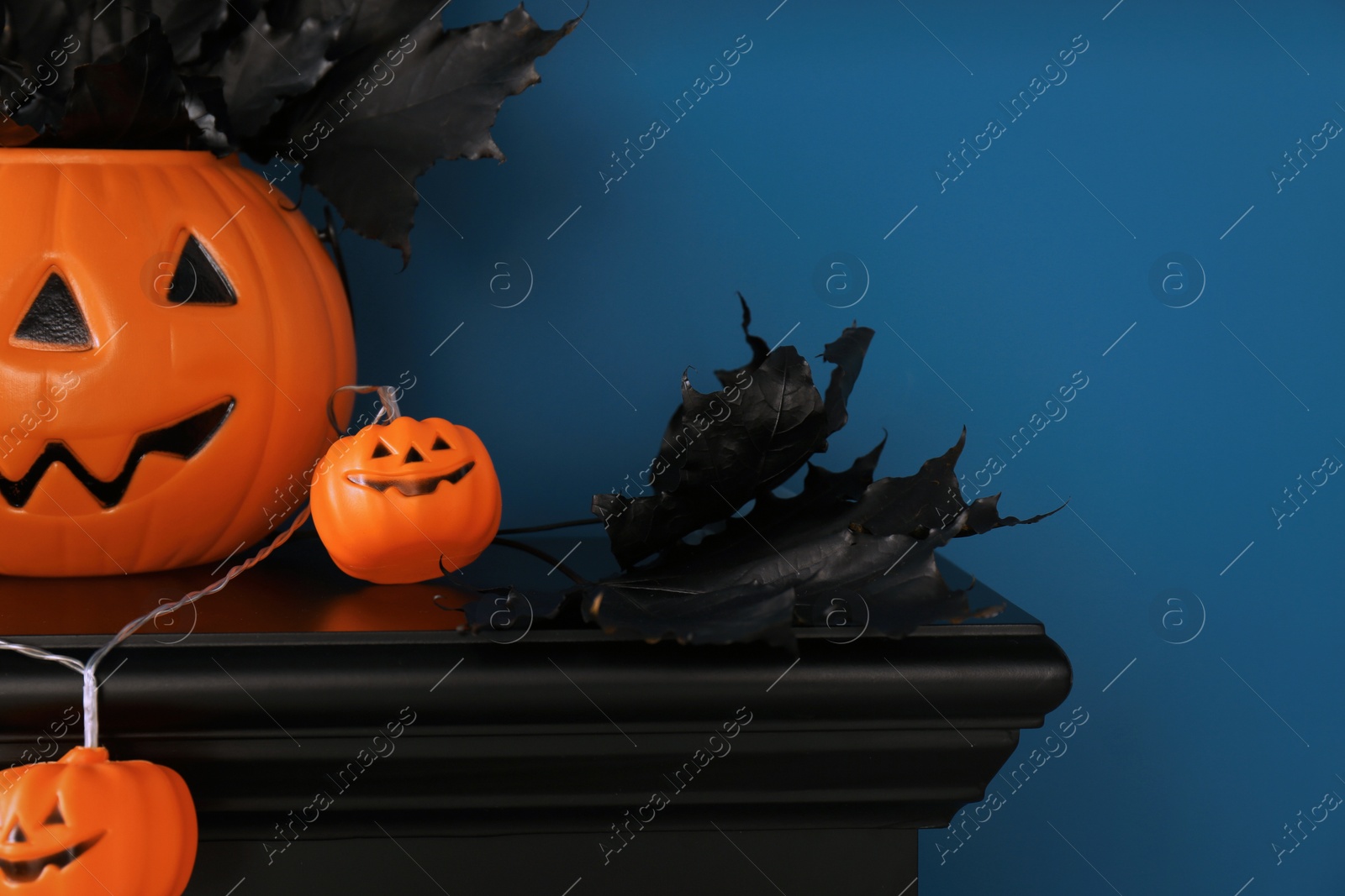 Photo of Jack-o'-lantern lights and black maple leaves on wooden fireplace near blue wall