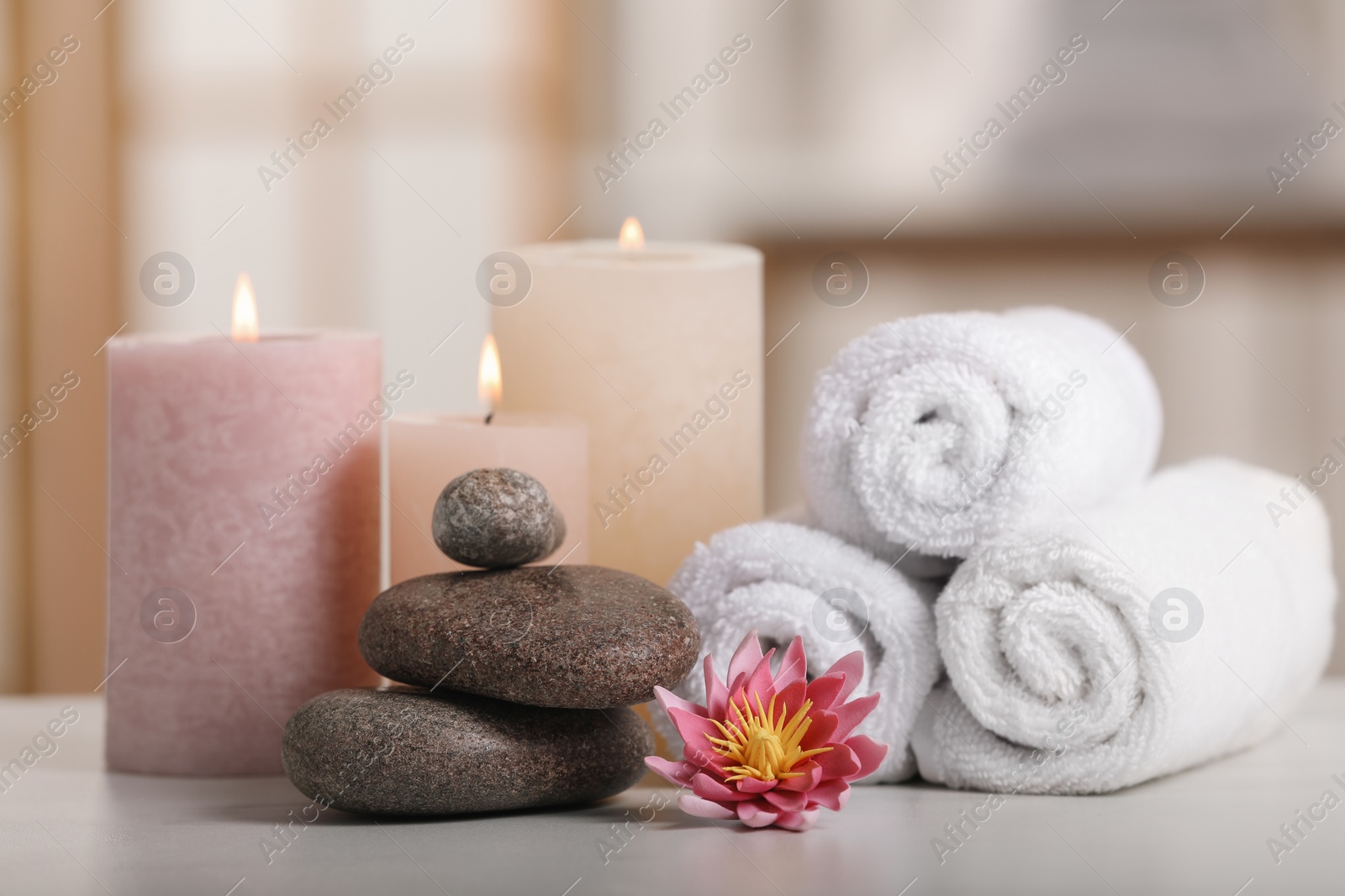 Photo of Spa composition. Burning candles, lotus flower, stones and towels on white table