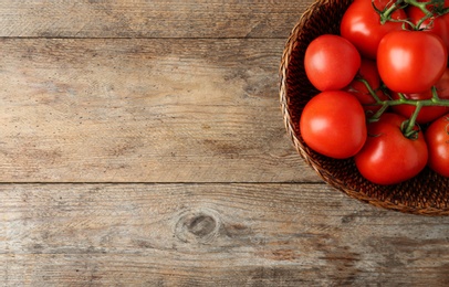 Photo of Fresh ripe red tomatoes in wicker bowl on wooden table, top view. Space for text