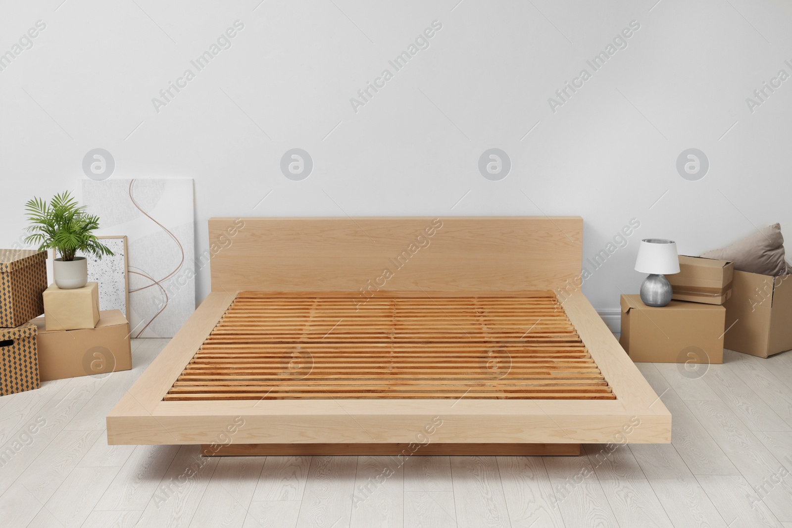 Photo of New wooden bed frame, moving boxes and decor elements indoors