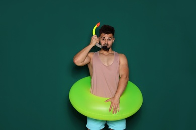 Photo of Funny young man with bright inflatable ring on dark green background