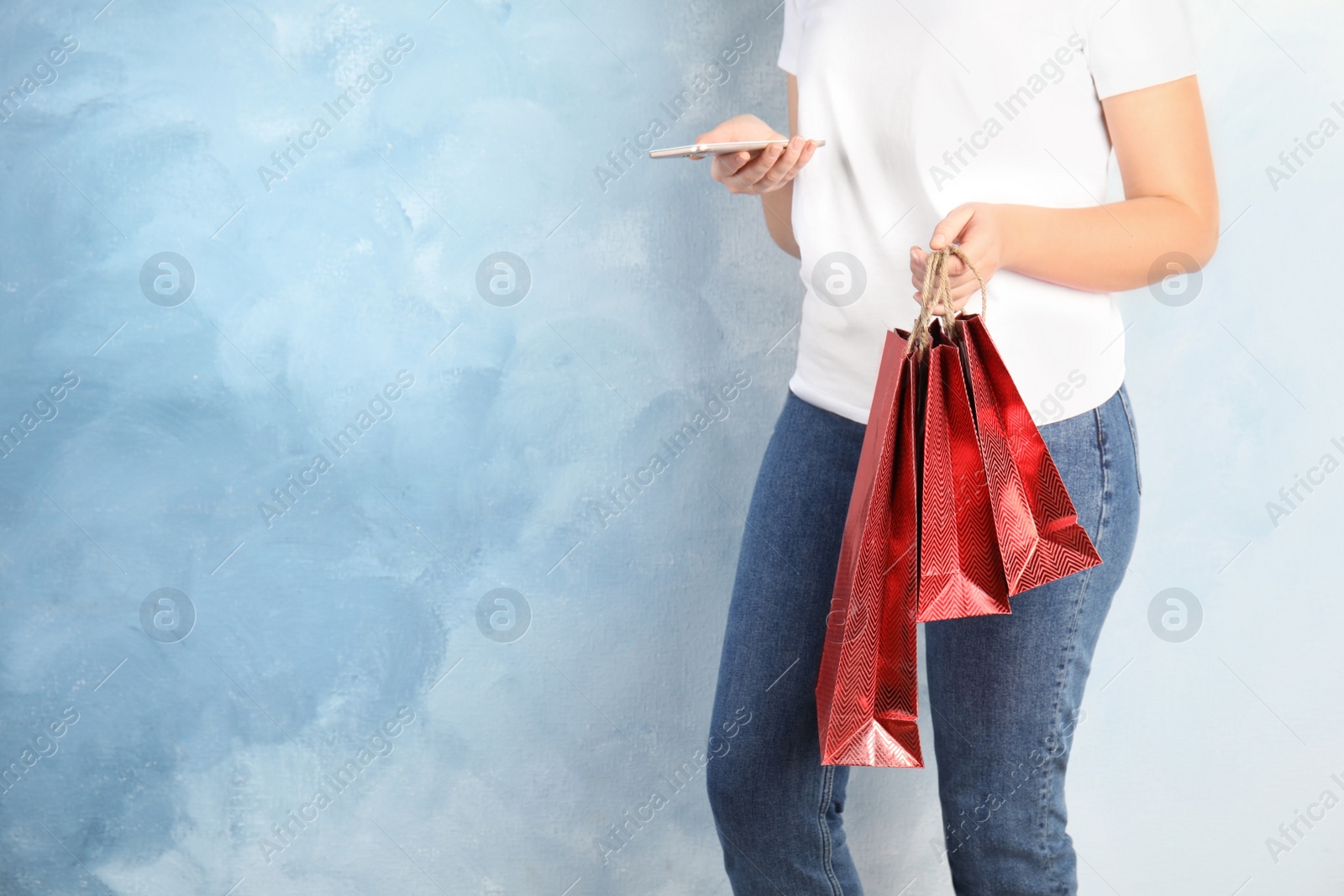 Photo of Woman with red shopping paper bags and smartphone on light blue background, closeup. Space for text