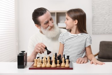 Photo of Senior man teaching his granddaughter to play chess at home